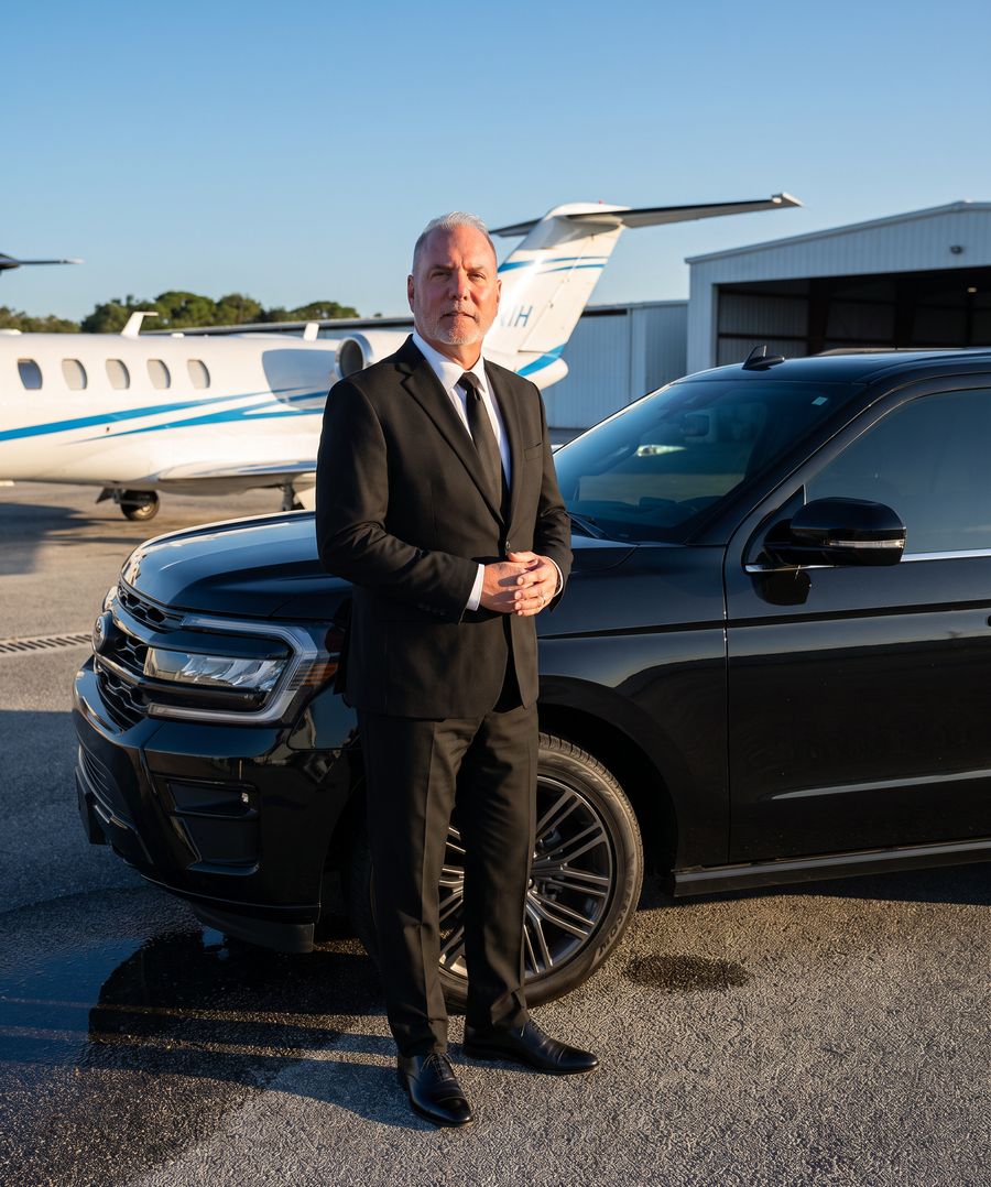 Jamie, owner and driver of J.R. Luxury, in a black suit beside his black Ford Expedition on a private aviation apron